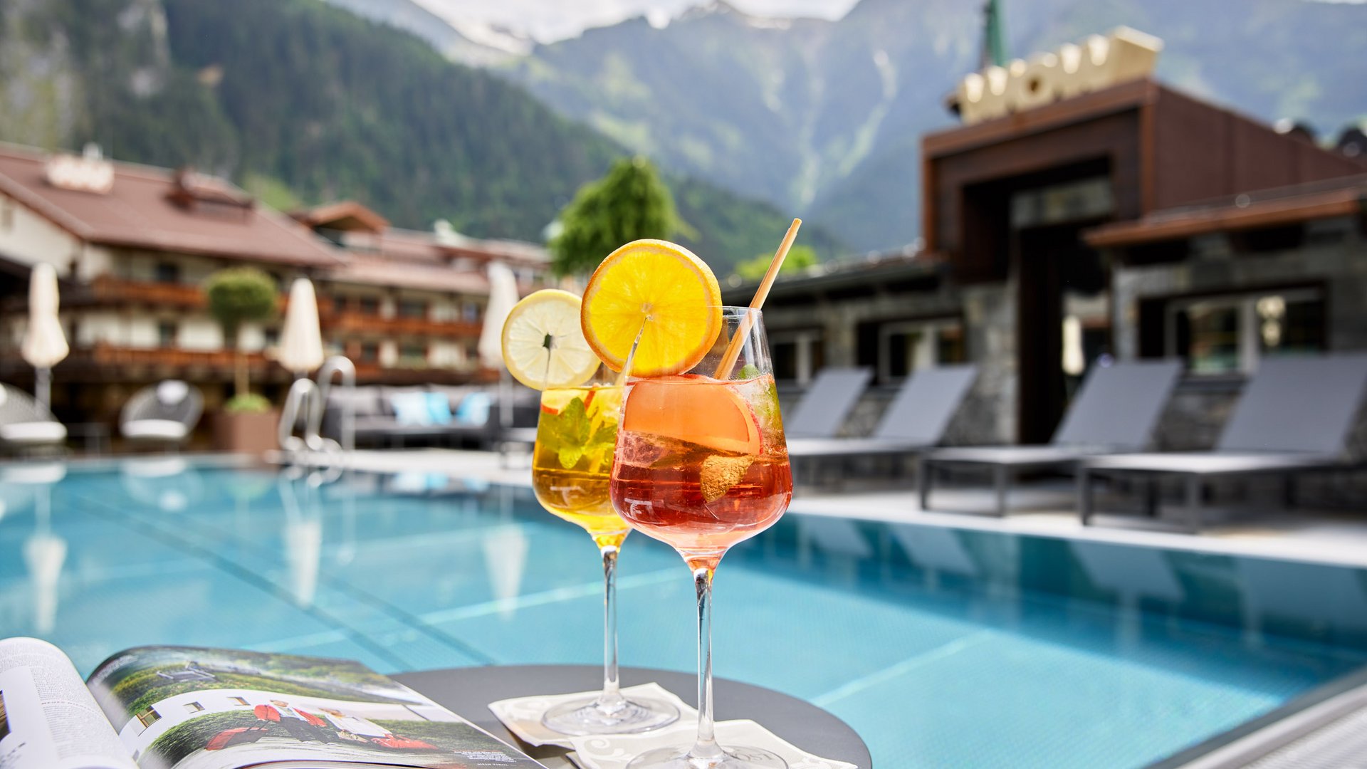 Zwei erfrischende Cocktails am Pool mit Bergblick und geöffnetem Magazin